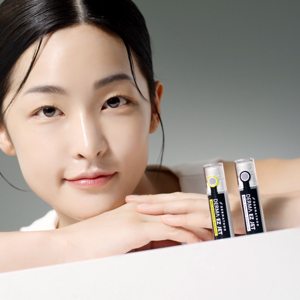 Koreanische Junge Frau lehnt an einen Tisch, auf dem zwei Dermathod Produkte stehen